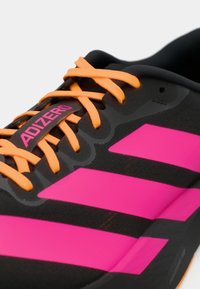 Közelkép fekete Adidas Adizero cipőről élénk rózsaszín csíkokkal és narancssárga fűzőkkel.