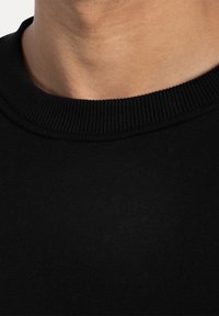 Černý pletený svetr s žebrovaným kulatým výstřihem. Materiál má hladkou texturu a těsný střih u krku, což zdůrazňuje elasticitu látky.