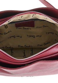 Borsa a mano in pelle rossa con zip sulla parte superiore. L'interno presenta una fodera beige con una stampa ripetuta "Pierre Cardin", incluso un taschino con zip.
