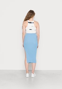 Top de tiras tie-dye branco com decote redondo, combinado com uma saia midi canelada azul clara com uma fenda lateral. Ténis brancos completam o visual.