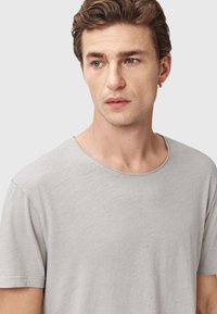 T-shirt grigio chiaro a maniche corte realizzato in tessuto morbido, con scollo rotondo e texture sottile. Nessun motivo o dettaglio visibile.