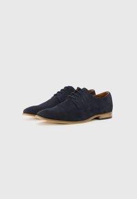 Chaussures habillées en daim bleu marine avec une texture lisse, bout pointu et semelle en caoutchouc marron clair. Présente un design à lacets et une couture minimale.