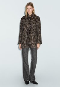 Nepvachtjas met zwarte en beige zebra-strepen, sluiting met één knoop, zijzakken, gecombineerd met donkere spijkerbroeken en zwarte schoenen.
