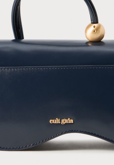 Tumed sinine nahast käekott, millel on sile tekstuur. Omab kullakarva ümmargust aktsenti ja "Cult Gaia" logo kuldsete tähtedega esiküljel.
