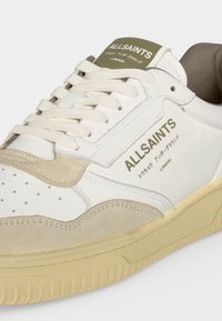 Λευκό και μπεζ sneaker AllSaints με κορδόνια, διάτρητο μπροστινό μέρος και σήμανση στα Αγγλικά και Ιαπωνικά στο πλάι και στη γλώσσα.