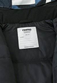 Schwarze wasserdichte Jackeninnenseite mit einem Stofflabel; enthält "Reima", Größe 104/4T und Pflegehinweise, die auf dem Etikett gedruckt sind.