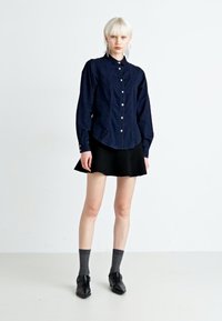 Camicetta blu navy con colletto, maniche lunghe e tessuto testurizzato abbinata a una gonna a ruota nera, calzini grigi e scarpe nere.