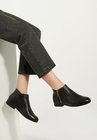 Black ankle boots with a textured finish, low heel, side zipper, and subtle croc pattern on one side. Worn with cropped jeans.