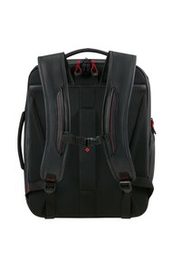 Mochila negra con correas de hombro acolchadas, tela de malla, acentos rojos y hebilla de pecho ajustable. Cuenta con un asa superior para llevarla.