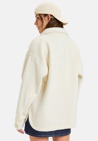 Cremefarbene Fleecejacke mit strukturierter Oberfläche, übergroßer Passform und Kragen. Verfügt über Seitenschlitze und Knopfdetails.