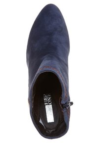 Bottine en daim bleu marine avec bout pointu, fermeture éclair visible sur le côté et détail de surpiqûres marron contrastantes.