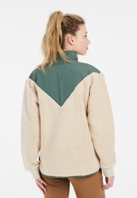 Fleece jacket in beige met een groene nylon bovenkant en kraag. Het heeft een ontspannen pasvorm en ribgebreide manchetten, met een gestructureerd oppervlak.