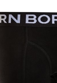 Črne bombažne bokserice s širokim elastičnim pasom, na katerem je bel napis "BORN". Gladka tekstura, prilegajoča oblika in ojačani šivi.