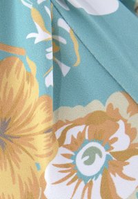 Tessuto floreale con grandi fiori gialli, bianchi e turchesi su uno sfondo blu chiaro, con una finitura strutturata e leggermente lucida.
