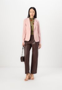 Pink blazer, floral green top, dark brown faux leather wide-leg pants, and nude heels. Model holds a small brown handbag.