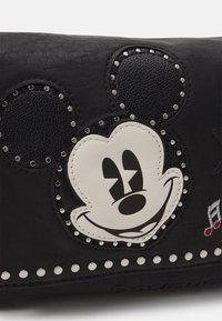 Schwarze Lederbrieftasche mit strukturiertem Oberflächen, Applikation eines lächelnden Cartoon-Charakters und Metallnieten entlang der unteren Kante.