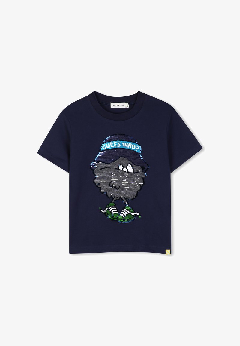 Μπλε ναυτικού κοντομάνικο t-shirt με ένα παγιετένιο καρτούν πρόσωπο που φοράει καπέλο με την επιγραφή "GUESS WHO?" και πράσινα αθλητικά παπούτσια.