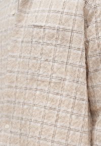 Μπεζ πουκάμισο με καρό σχέδιο, λεπτές καφέ και λευκές ρίγες, με τσέπη στο στήθος και κουμπιά σε κρεμ απόχρωση.