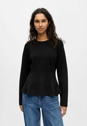 Schwarzes langärmeliges Oberteil mit Peplum-Design, runder Ausschnitt und glattem Stoff. Kombiniert mit locker sitzenden Jeans.