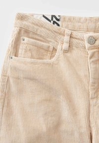 Beige Cordhosen mit senkrechter Rippstruktur, Fünf-Taschen-Design, Knopfverschluss und markiertem Taillenlabel.