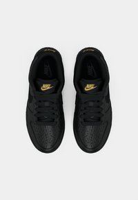 Juodi Nike sportbačiai su tekstūruotu paviršiumi, perforuotomis detalėmis, juodomis raištelėmis ir auksiniu logotipu ant liežuvėlio. Guminis padas.