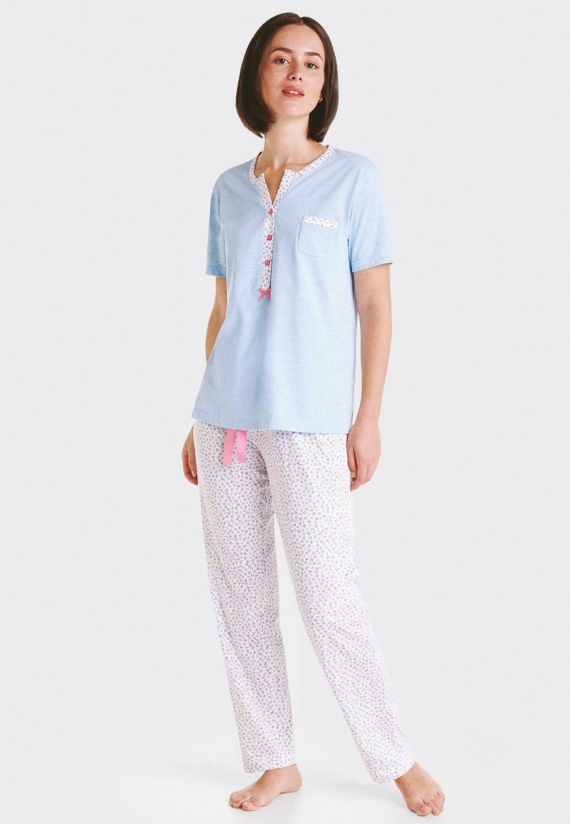 Top corto de manga corta azul claro con un collar y bolsillo con un patrón floral, combinado con pantalones blancos que cuentan con pequeños diseños florales coloridos y una corbata rosa.