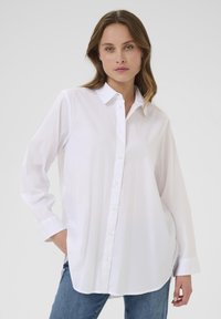 Camicia bianca con bottoni, maniche lunghe, realizzata in tessuto liscio, con colletto classico, pattina frontale e vestibilità rilassata.