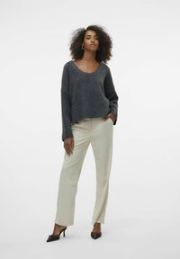 Gehaakte, donkergrijze trui met een wijde halslijn en lange mouwen, gecombineerd met lichtbeige, losse ribbroek en puntige hakken.
