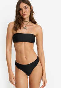 Μαύρο μπαντό τοπ μπικίνι, με ταιριαστό σλιπ μπικίνι σε χαμηλή μέση. Λείο, ελαστικό ύφασμα με ελάχιστα ραφές, με απλό σχέδιο.