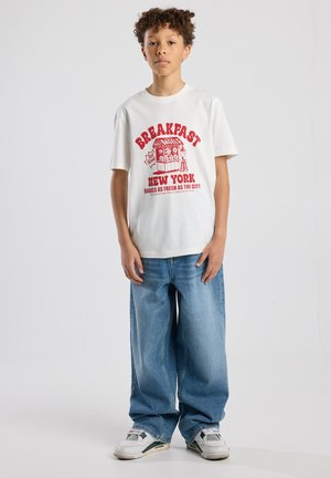 White cotton t-shirt with red graphic text "BREAKFAST NEW YORK" and bagel illustration, paired with wide-leg blue jeans and sneakers.