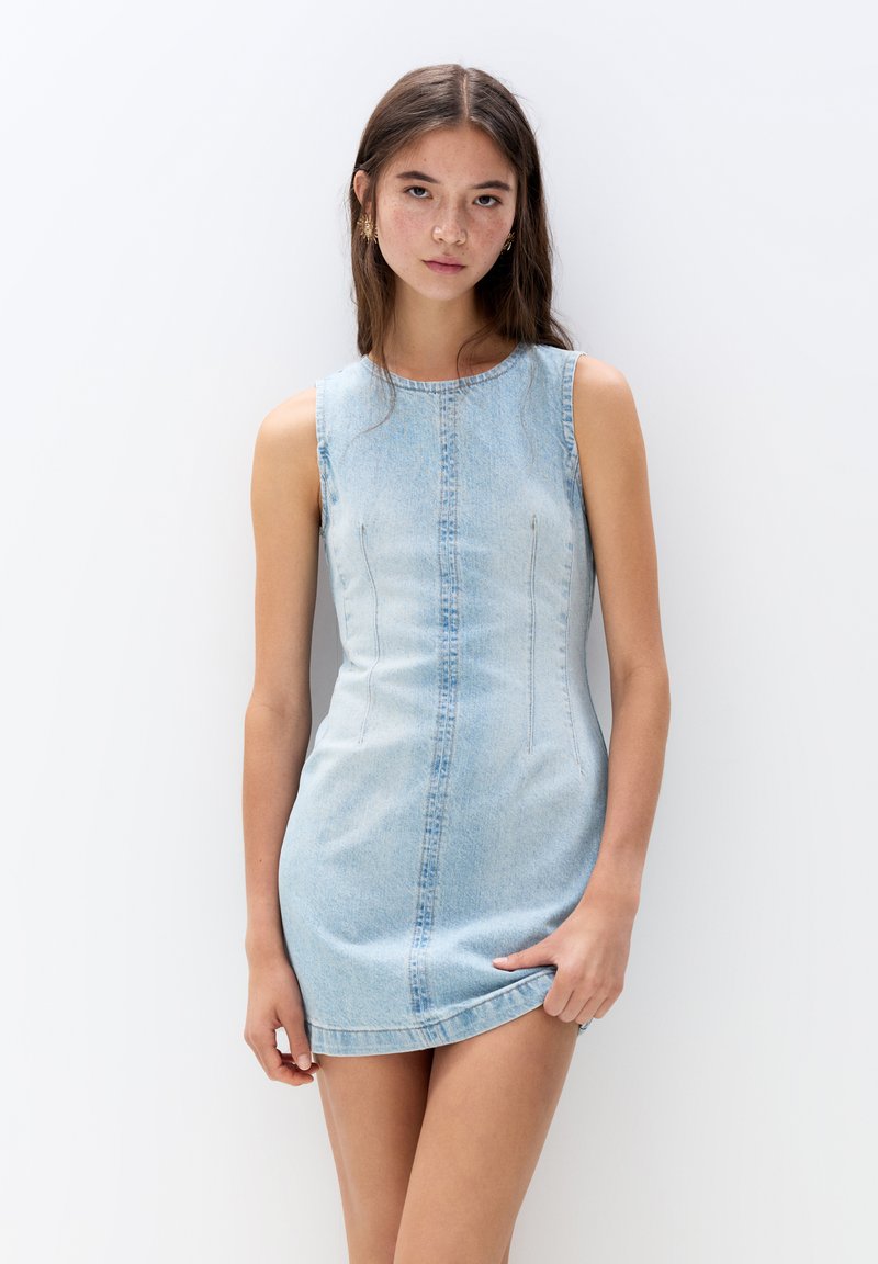 Denim mini haljina svijetloplave boje, bez rukava, s uskim krojem, zakrivljenim izrezom i suptilnim vertikalnim detaljima šivanja.
