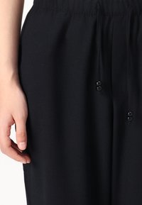 Pantaloni neri con cordoncino realizzati in tessuto morbido, con una vita elasticizzata e accenti in corda nera e superficie textured.