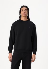Schwarzes Sweatshirt aus weichem Stoff, mit Rundhalsausschnitt, langen Ärmeln und einem kleinen weißen Logo auf der Brust.