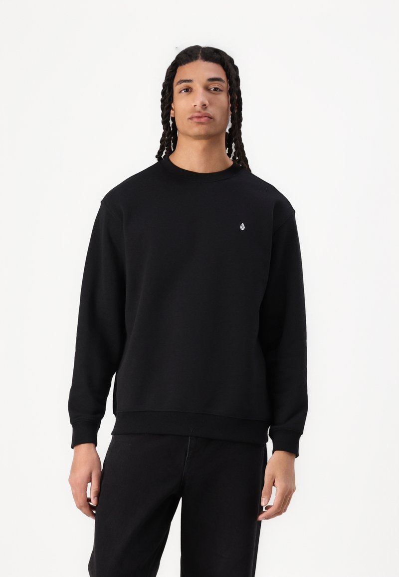Schwarzes Sweatshirt aus weichem Stoff, mit Rundhalsausschnitt, langen Ärmeln und einem kleinen weißen Logo auf der Brust.