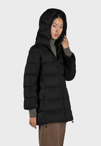 Giacca imbottita nera con cappuccio, dotata di chiusura con zip e due tasche laterali. Il tessuto appare liscio con una texture trapuntata.