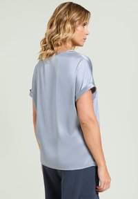 Lichtgrijze blouse met korte mouwen, gemaakt van gladde, glanzende stof. Heeft opgerolde mouwen en een losse snit. Geen zichtbare patronen of accenten.