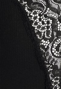 Black top featuring ribbed texture with intricate black lace detailing on one side, highlighting a floral pattern and scalloped edges.