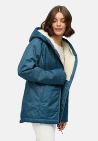 Niebieska kurtka przypominająca denim z kapturem, wyłożona kremowym sztucznym futerkiem i zapinana na zamek z przodu. Posiada boczne kieszenie i nieco dłuższy krój.