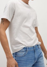 Camiseta de algodón blanca con mangas cortas, que presenta un corte relajado. Combinada con jeans de mezclilla azul claro que exhiben un corte clásico y un sutil desgaste.