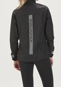 Chaqueta cortavientos negra con acentos reflectantes y un logo vertical de "ENDURANCE" en la parte trasera. Fabricada con un material ligero y suave.