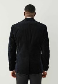 Marineblauwe suède blazer met een getailleerde pasvorm, een enkele split aan de achterkant en knopen bij de mouwen. Soepele textuur en verfijnd ontwerp.