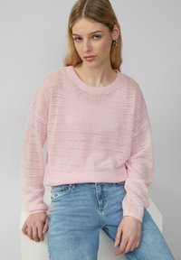 Lichtroze gebreide trui met een losse pasvorm, voorzien van een ronde halslijn en een gemêleerd patroon. Gecombineerd met lichtblauwe denim jeans.