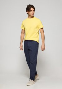 Camiseta de algodón amarilla, de manga corta, cuello redondo; pantalones navy de corte recto; zapatillas beiges. Diseño sencillo sin estampados.