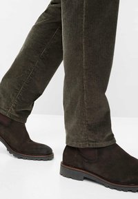 Bordeaux kleurige suède enkellaarzen met een textuurafwerking, gecombineerd met olijfgroene corduroy broek met verticale ribbels.