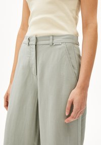 Helle grüne, weite Hosen mit glatter Textur, ausgestattet mit einem Gürtel mit Schlaufen und einem kleinen Etikett am Bund.