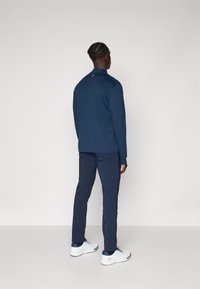 Navy long-sleeve top with a stand collar, paired with navy pants and white athletic shoes. Smooth fabric, minimal detailing, and a relaxed fit.