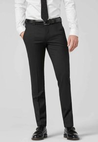 Schwarze Anzughosen mit schmaler Passform, aus glattem Stoff, mit flacher Vorderseite, Gürtelschlaufen und scharfen Falten. Kombiniert mit schwarzen Schuhen.