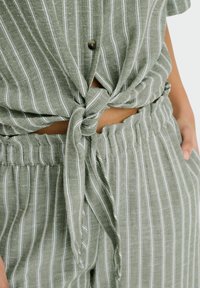 Groen gestreepte stoffen set bestaande uit een geknotte shirt en elastische broek, gemaakt van lichtgewicht materiaal met contrasterende witte strepen.