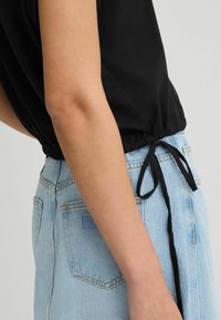 Zwarte top met elastische tailleband en strikdetail, gecombineerd met een lichtblauwe denim rok met achterzakken en label.