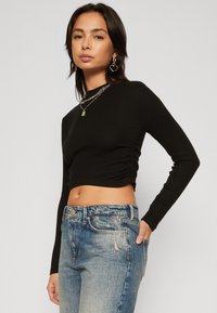 Crni rebrasti dugoruki crop top s okruglim izrezom, uparen s izblijedjelim plavim trapericama visokog struka koje imaju kopčanje na dugme i džepove.